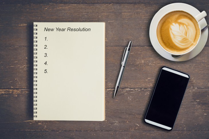 Business concept - Top view notebook writing New Year Resolution, pen, coffee cup, and phone on wood table.